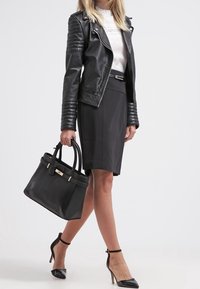 Svart läderjacka med quiltade ärmar, vit blus, svart pennkjol och svart handväska. Modellen bär svarta spetsiga klackskor.