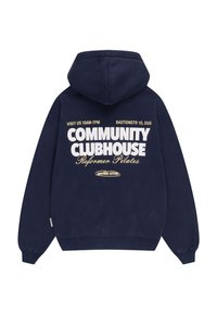 Sweat à capuche bleu marine avec capuche, manches longues, et texte blanc et beige indiquant "Community Clubhouse Reformer Pilates" ainsi que les heures d'ouverture et l'adresse du magasin.