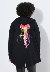 Sudadera negra de manga larga, con un gráfico colorido de medusa en la parte posterior en tonos rosa, amarillo y verde, con dobladillo redondeado y cordón ajustable.