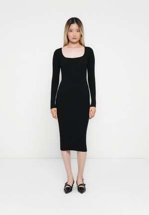 Black ribbed midi dress with long sleeves and a square neckline, featuring a fitted silhouette and smooth texture. Worn with black pointed shoes.