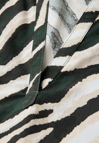 Zebra print fabric featuring green and beige stripes, with a textured surface. The design includes a V-neckline and neat stitching.