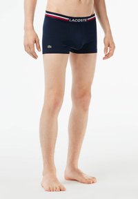 Boxers en coton bleu marine avec une ceinture renforcée ornée de rayures rouges et blanches et un petit logo Lacoste vert sur le devant.