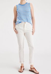 Randig blå och vit ärmlös topp i kombination med krämfärgade, figurnära byxor. Klädseln kompletteras med bruna platta sandaler.