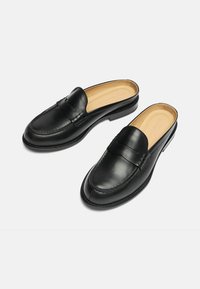 Crne kožne loafer cipele bez vezivanja s zaobljenim vrhom, dekorativnim šavovima, suptilnim detaljem remena i glatkom završnom obradom. Ravni gumeni đon.