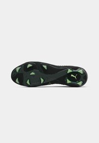 Puma soccer cleat bottom view, featuring a black textured sole with green accents and distinct traction studs designed for grip.