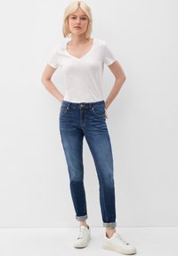 Jeans ajustados de mezclilla en color azul, con un ligero desgaste, cinco bolsillos y dobladillos enrollados. Llevados con una camiseta blanca de cuello en V y zapatillas blancas.