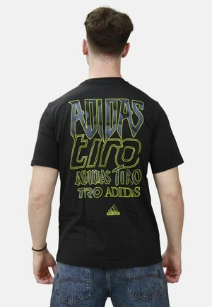 Zwart katoenen t-shirt met grote gele grafische tekst op de rug, met "ADIDAS" en "TIRO" duidelijk weergegeven.