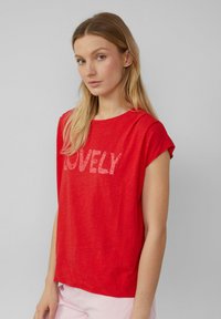 T-shirt rouge à manches courtes avec une coupe décontractée et le mot "LOVELY" imprimé en gris clair sur le devant. Tissu doux et léger.