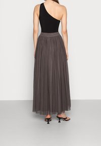 Schwarzer Ein-Schulter-Body kombiniert mit einem langen, fließenden, dunkelgrauen Tüllrock. Der Rock verfügt über ein gerafftes Design und einen verdeckten Reißverschluss in der Taille.