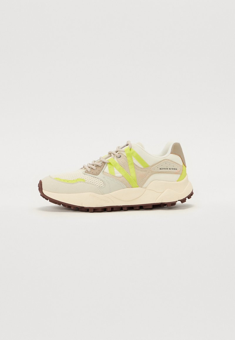 BeigeSneaker aus Mesh- und Wildledermaterialien, mit leuchtend gelben Akzenten, einer dicken Sohle und strukturierten Mustern im oberen Bereich.