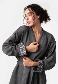 Šedý župan s dlhými rukávmi, textúrovaná tkanina a kontrastné vzorované manžety. Obsahuje opasok na viazanie v páse.