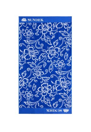 Asciugamano Sundek blu con fiori di ibisco bianchi e foglie che si avvolgono, con testo e logo "SUNDEK" sui bordi superiore e inferiore.