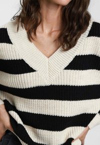 Maglione lavorato a maglia con scollo a V, caratterizzato da strisce orizzontali alternate nere e crema; tessuto testurizzato, vestibilità ampia e maniche larghe.