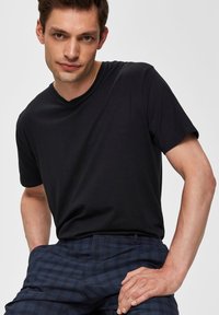 Camiseta negra de cuello en V con mangas cortas, hecha de una tela suave. Combinada con pantalones de cuadros azul oscuro, que presentan un corte relajado y bolsillos laterales.