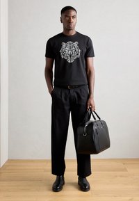 Zwarte t-shirt met een gedetailleerde tijgerafbeelding, gecombineerd met losse zwarte broeken en een elegante zwarte leren tas. Soepele textuur, modern ontwerp.