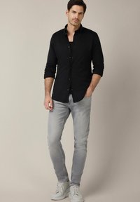Czarna koszula z długim rękawem, dopasowana, z zapięciem na guziki. Noszona z jasnoszarymi dżinsami slim fit i białymi trampkami. Gładki materiał, minimalne akcenty.
