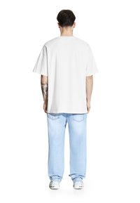 Biała bawełniana koszulka z krótkim rękawem, zestawiona z jasnoniebieskimi dżinsami, noszona z białymi trampkami. Widok z tyłu.