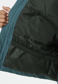 Türauskleidung in Türkis mit dunkelgrüner Fütterung, die eine glatte Textur aufweist und einen elastischen Bund am unteren Rand hat. Reißverschlussdetails sind sichtbar.