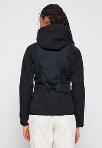 Czarna kurtka outdoorowa z kapturem, z teksturowanym niebieskim panelem tylnym, elastycznymi mankietami i dopasowaną talią dla uzyskania smukłego kształtu.