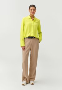 Camisa de manga larga a rayas verde lima con botones al frente, combinada con pantalones beige de cintura alta y zapatillas blancas. Cinturón negro de acento.