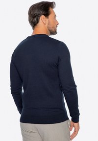 Maglione lavorato a maglia blu navy con maniche lunghe, polsini e orlo a coste, caratterizzato da un collo tondo e una texture liscia, visto da dietro.