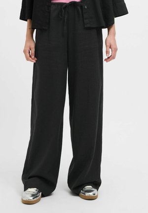 Zwarte wijde broek gemaakt van lichte stof met een trekkoord in de taille, gecombineerd met zilveren sneakers met een textuurafwerking.