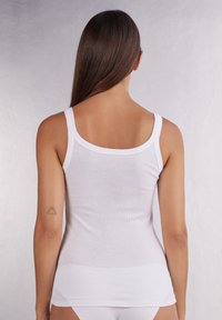 Witte geribde tanktop met brede schouderbanden, aansluitende pasvorm, zachte textuur en een ronde rugontwerp. Kenmerkt zich door een gladde, naadloze uitstraling.
