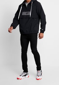 Černá mikina s kapucí s předním logem, nastavitelnou kapucí a elastickými manžetami, doplněná úzk ými černými džíny a víceduho barevnými teniskami.