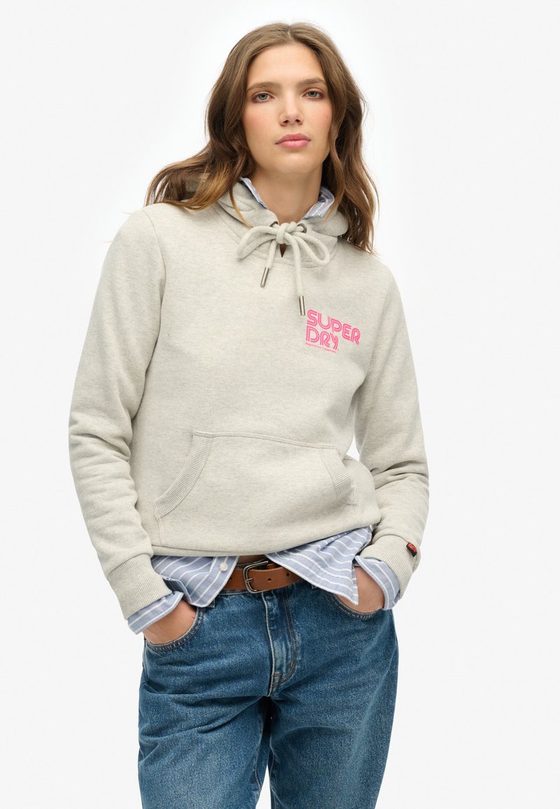Lichtgrijze hoodie met trekkoord, roze "SUPERDRY" logo en een voorkelet. Draagt over een blauwgestreept shirt en gecombineerd met high-waisted jeans.