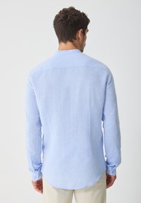 Light blue long-sleeve shirt made of fabric with a textured finish. Features a standard collar, button cuffs, and a curved hemline.