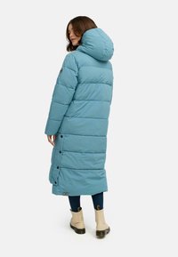 Lang, lys blå pufferjakke med hette, med horisontale sømmer, trykknapper på siden og en lett innsnidd passform nederst.