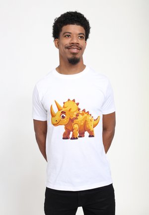Homme debout et souriant, portant un t-shirt blanc avec un dessin coloré de tricératops de dessin animé sur le devant.