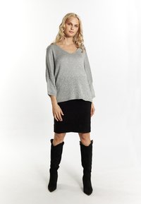 Maglione argento a maglia con scollo a V e maniche tre quarti, abbinato a una gonna a tubino nera e stivali alti in suede neri.