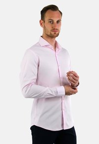 Lichtroze overhemd met lange mouwen, een puntkraag, knoopsluiting aan de voorkant en een getailleerde pasvorm. Soepele textuur, gecombineerd met donkere broek.