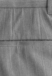 Tissu à motif pied-de-poule en noir et blanc avec une texture lisse. Présente des plis et une taille plate, mettant en avant un design classique.