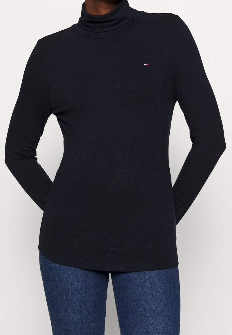 Svart ribbad turtleneck med långa ärmar, med en liten logotypdetalj. Tillverkad av ett mjukt, elastiskt material.