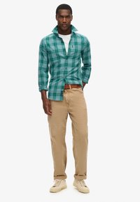 Camicetta a quadri verdi con colletto, abbinata a pantaloni beige e sneakers crema. La camicia presenta maniche lunghe e una vestibilità dritta.
