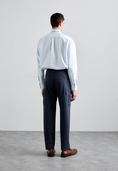 Camisa de manga larga azul claro con cuello abotonado, combinada con pantalones cargo azul marino con bolsillos laterales, y zapatos de cuero marrón.