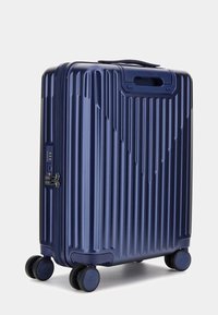 Marineblauer Hartschalenkoffer mit vertikalen Rillen, seitlichem Griff, integriertem Zahlenschloss und vier schwarzen Spinner-Rollen für einfache Mobilität.
