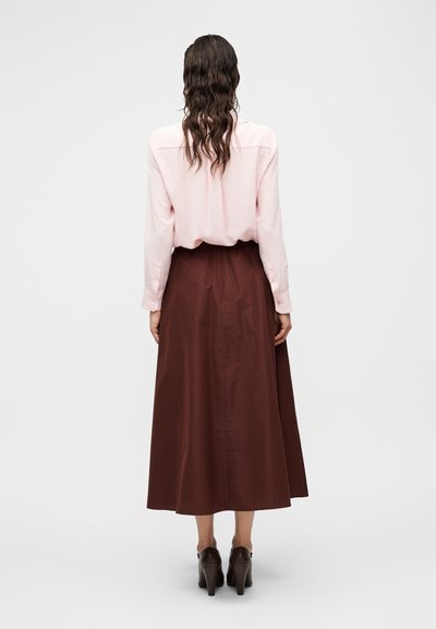 Ροζ πουκάμισο με κλασικό γιακά, σε συνδυασμό με καφέ, αέρινη μακριά φούστα, και τα δύο από απαλό ύφασμα, συνοδευόμενα από σκούρα παπούτσια με τακούνι.