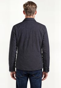 Mørkeblå quiltet jakke med notched krave, med et bølget søm mønster på ryggen og knappede mansjetter. Glat overflade, skræddersyet pasform.