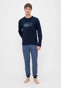Camisa de manga larga azul marino con el logo de Lacoste; pantalones de pijama estampados en tonos azules, con diseño repetitivo del logo; material de algodón.