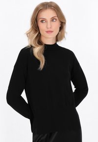 Schwarzer Pullover mit hohem Kragen, langen Ärmeln, Seitenschlitzen, geripptem Saum und lockerer Passform. Glattes Strickmaterial.