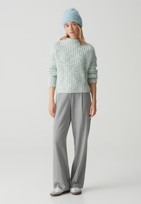 Maglioncino blu chiaro a collo alto, abbinato a pantaloni grigi a gamba larga e sneakers bianche. Il maglione ha un aspetto morbido e texture.