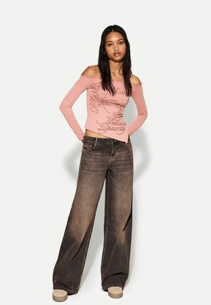 Top roz cu mâneci lungi și guler tip off-the-shoulder, cu text grafic; asortat cu blugi dark denim cu talie largă și încălțăminte bej cu platformă.