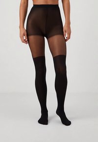 Μαύρες διάφανες καλσόν με ψηλή μέση, λεία υφή και αδιαφανή περιοχή στο πόδι. Σχεδιασμένες για άνεση και εφαρμοστή σιλουέτα.
