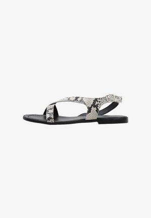 Sandalias planas con un diseño de estampado de serpiente en blanco y negro, con una tira cruzada y hebilla en el tobillo, fabricadas en un material sintético texturizado.