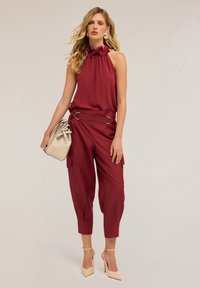 Top bordeaux a collo halter con dettagli arruffati abbinato a pantaloni cargo affusolati; la modella porta una borsa beige chiaro e indossa tacchi beige.
