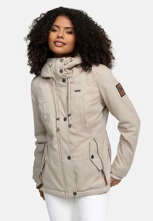 Beige waterdichte jas met een hoge kraag, ritszakken en een logopatch. Voorzien van verstelbare trekkoordjes en een knoopsluiting aan de voorkant.