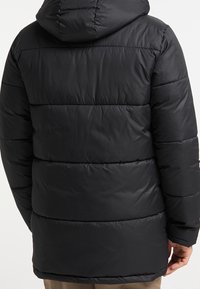Svart puffjacka med huva, med en kviltad design, horisontella sömmar och en slät, glansig yta. Mellanlång stil.